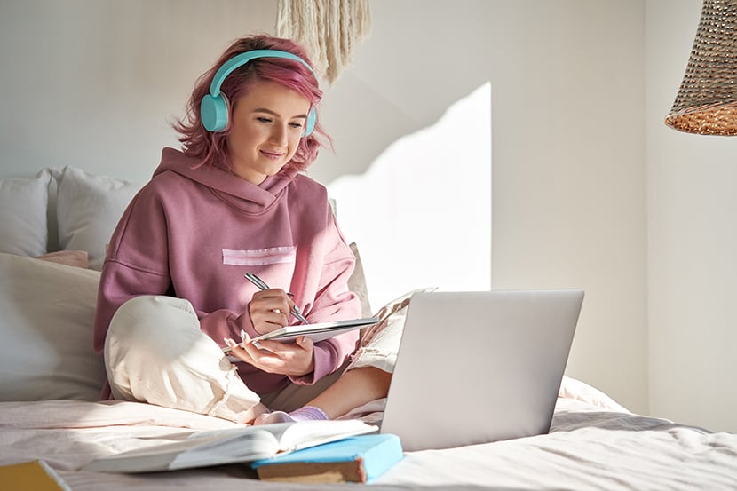 Student using a laptop on her bed with headphones