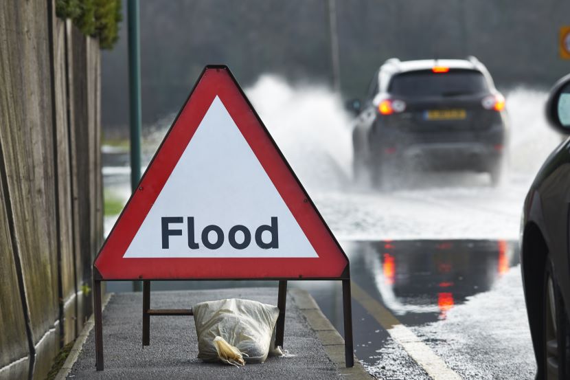 Car driving through floodwater near a flood road sign