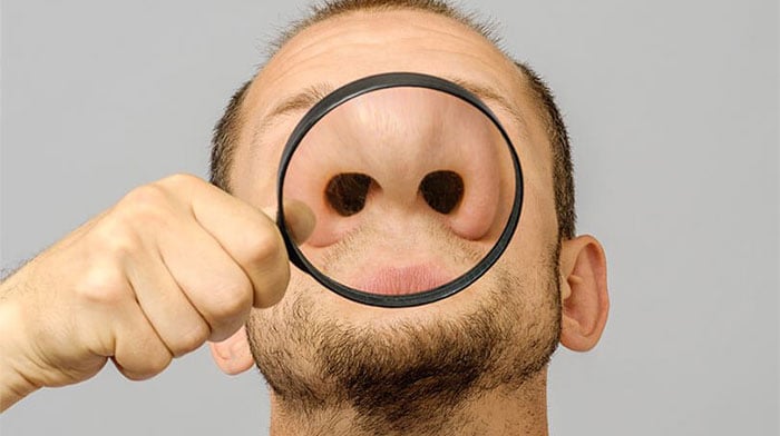 Man holding a magnifying glass up to his nose