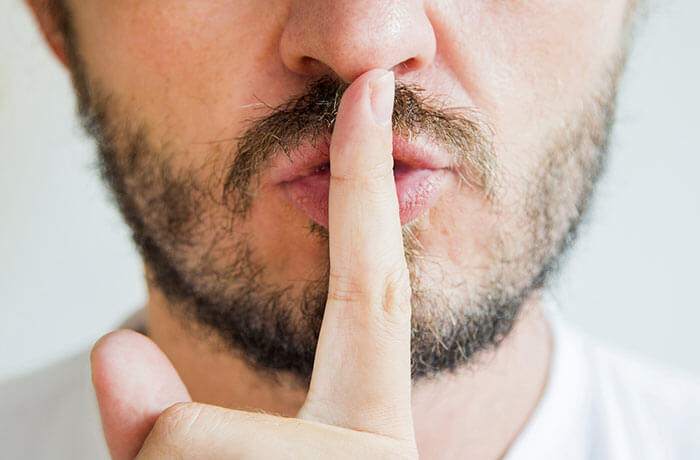 Bearded man with fingers on lips indicating quiet