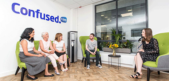 Confused.com staff sitting around the Confused.com logo
