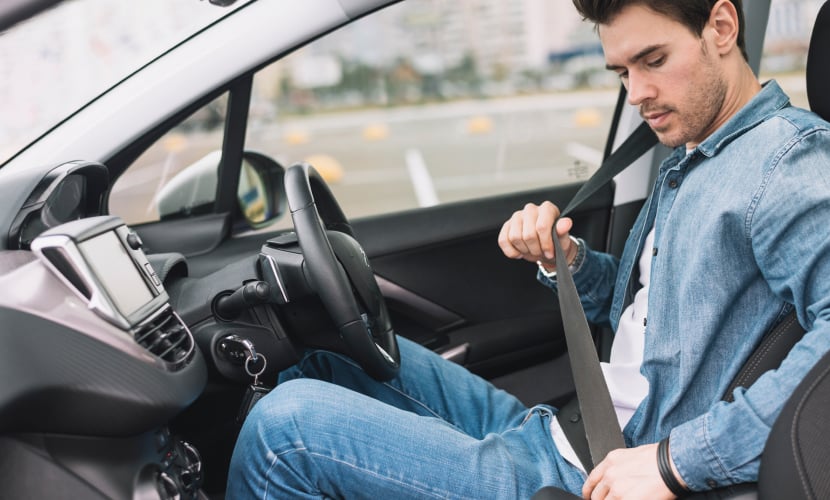 Someone sat in the driving seat of a car putting their seatbelt on