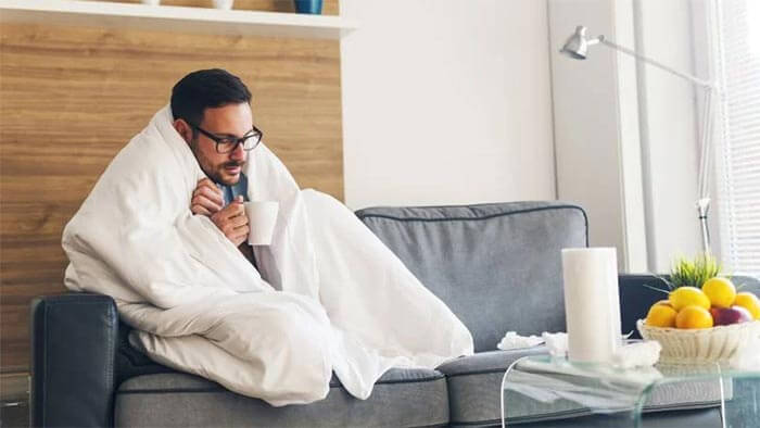 A man snuggled under a duvet with a cup of tea