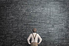 A person looking closely at a chalkboard covered in writing
