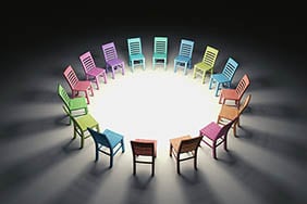 Different coloured chairs organised in a circle around a bright circle