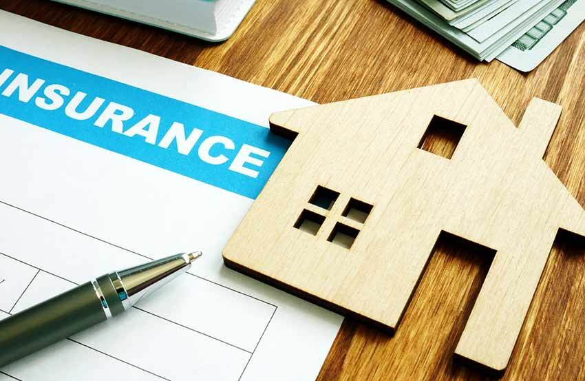 a wooden cut out of a house next to a pen on top of insurance documents