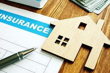 a wooden cut out of a house next to a pen on top of insurance documents
