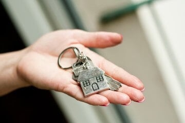 Closeup of a person giving metallic key with house shaped key chain to lodger