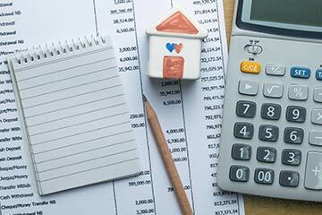 a notepad and pencil on table next to a calculator and model house