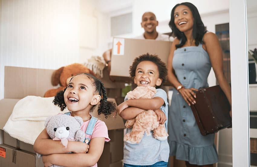 a family smiling and moving in to a home holding boxes