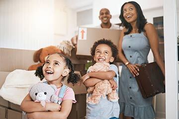 a family smiling and moving in to a home holding boxes