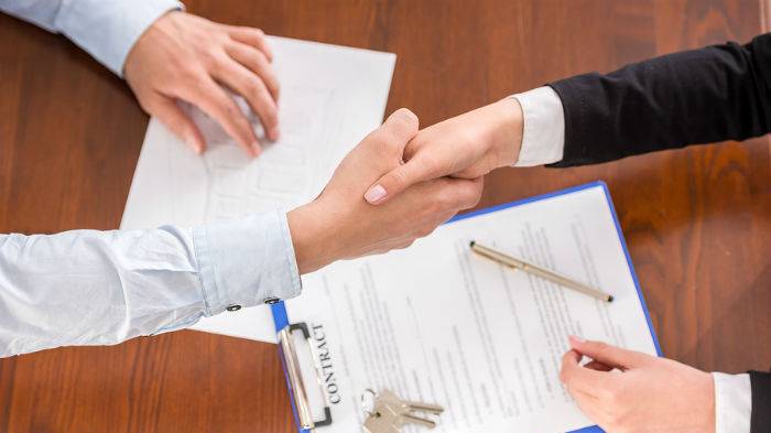 Two people shaking hands over paperwork and keys