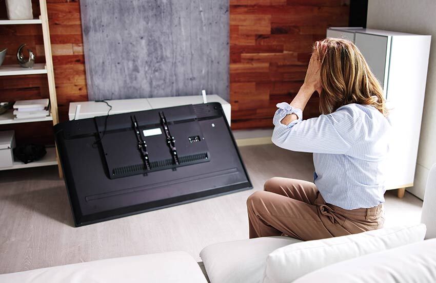 a person looking at a damaged tv with their hands on their head