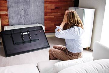 a person looking at a damaged tv with their hands on their head