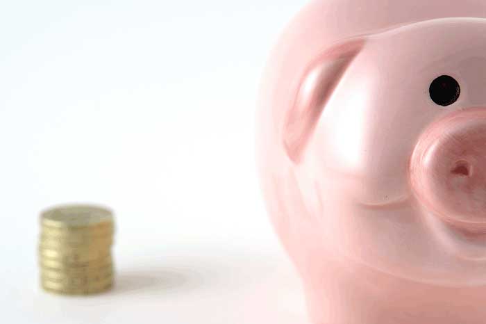 A close-up of a pig shaped piggy-bank with a stack of coins next to it