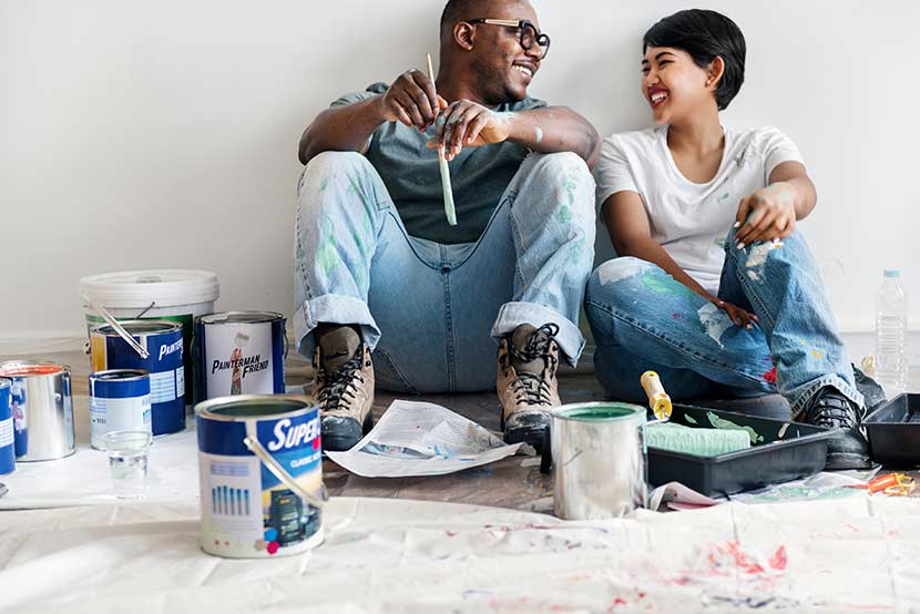 Smiling couple painting house wall