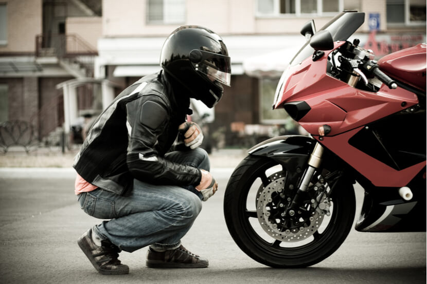 Biker wearing helmet kneeling in front of a motorbike