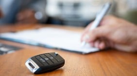 Someone signing paper work while car keys sit on the table eager to be used.