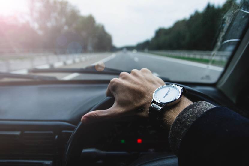 Drivers arm wearing a watch on wheel of a car driving along a straight road