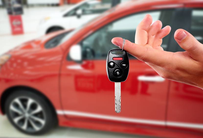 hand dangling car keys by red car in car showroom