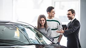 Couple looking at a car in a showroom while a car salesman looks on