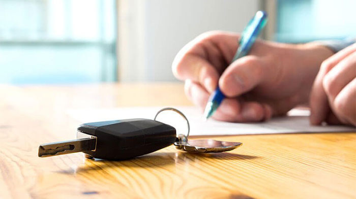 A set of car keys on the table while a hand fills in some paperwork