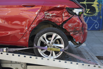 red car with smashed bumper loaded ready to be towed
