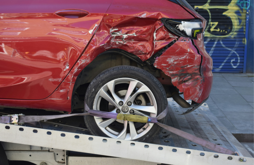 Red car with smashed bumper loaded ready to be towed