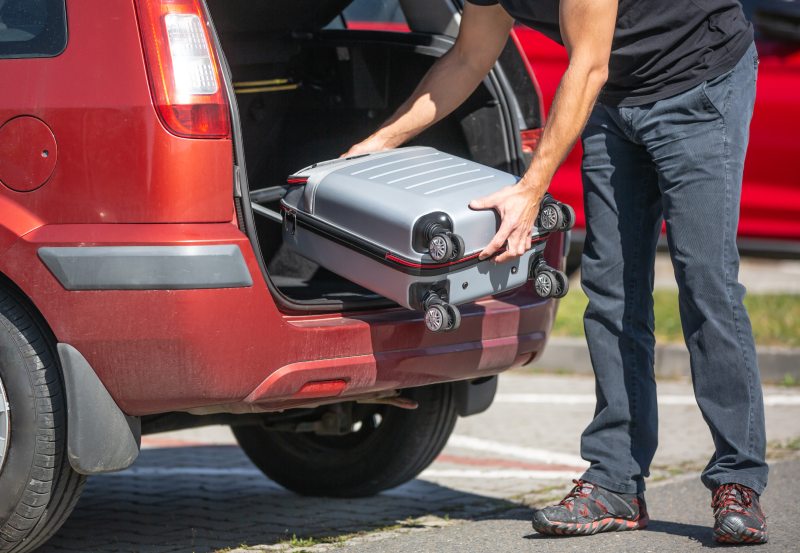 A driver abroad puts a suitcase in their hire car