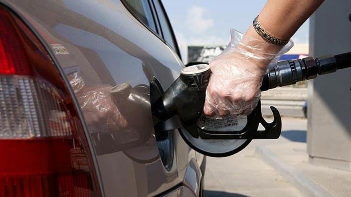 Hand holding a petrol pump while wearing disposable gloves