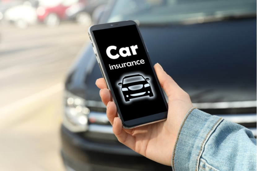 A person goes to a car insurance website on their phone, standing in front of a black car
