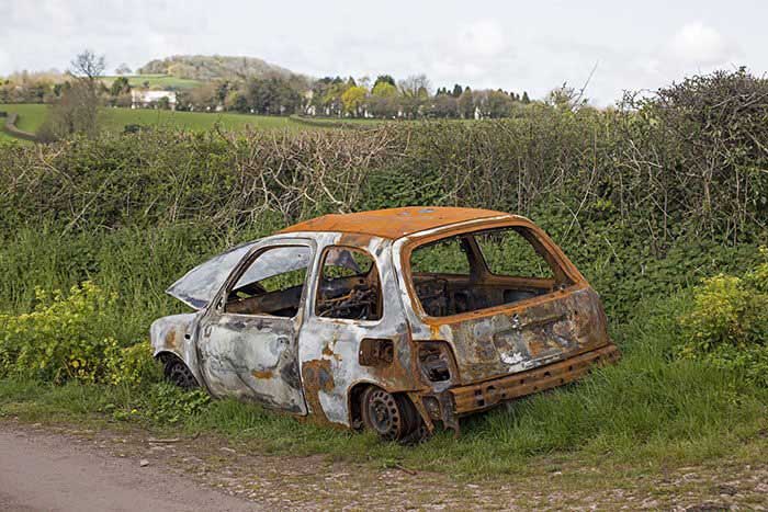 A rusted abandoned car on the side of the road