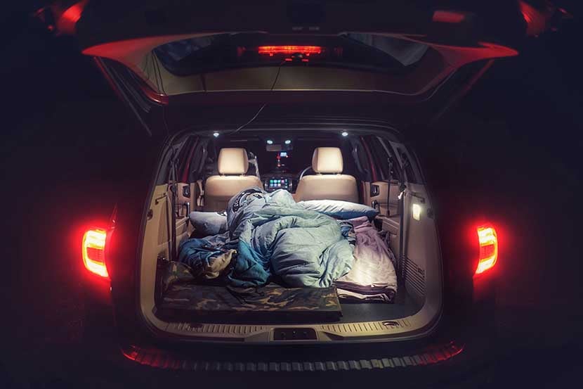 A bed is arranged in the back of a car for someone to sleep in 