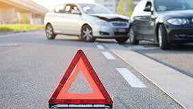 A red warning triangle in the foreground with a road traffic accident in the background