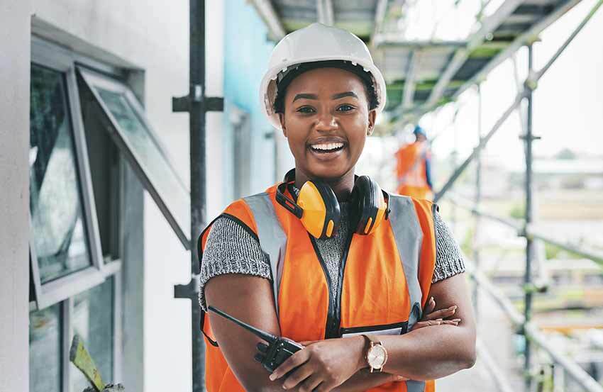 Builder with walkie-talkie in hand standing on scaffolding wearing a hi-vis jacket and smiling into camera