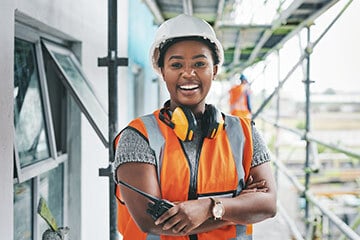 Builder in hard hat and hi-vis jacket standing on scaffolding structure and smiling into camera