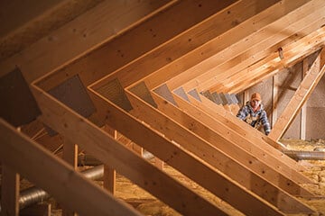 Worker inspecting wooden beams in a house's attic