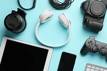 Gadgets including headphones, a tablet, a mobile phone and more laid out on a light blue background