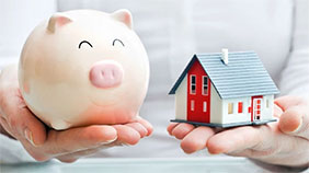 Hands holding a ceramic piggy bank and a model house