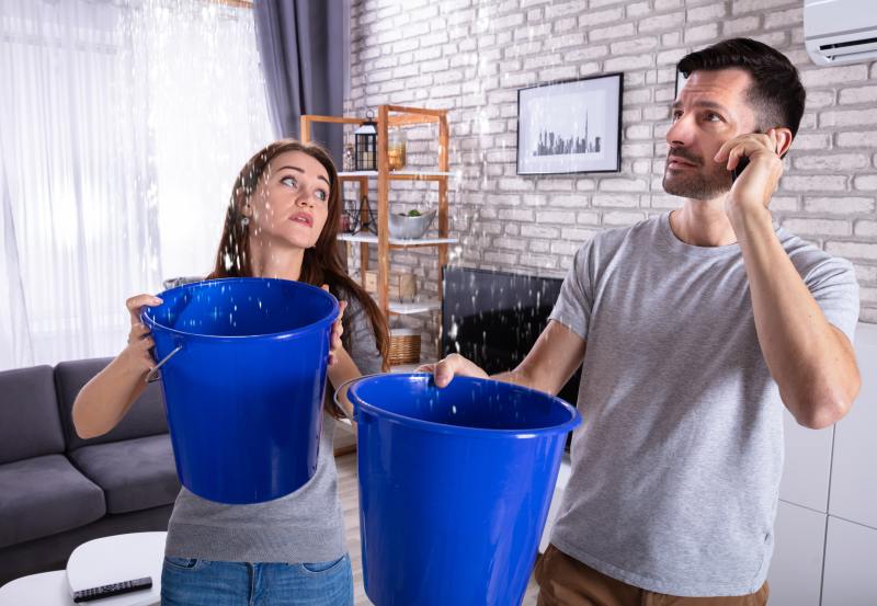 Two tenants holding a bucket for a leaking ceiling 