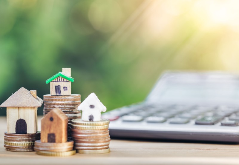 Toy houses sit on piles of money representing home excess