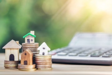 Toy houses sit on piles of money representing home excess