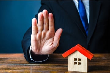 A model house representing home insurance with a broker signalling that it is invalid 