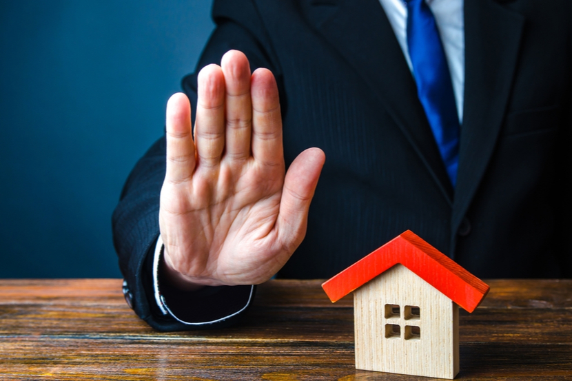 A model house representing home insurance with a broker signalling that it is invalid 