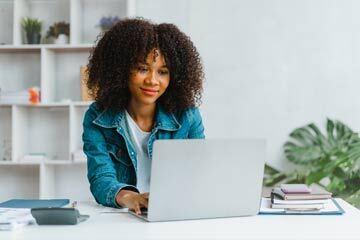 Woman using a laptop in a minimalist, white room with a plant in the background