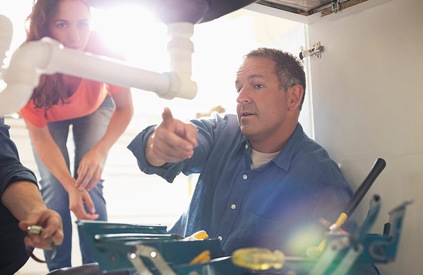 Plumber pointing out a pipe to woman standing behind him