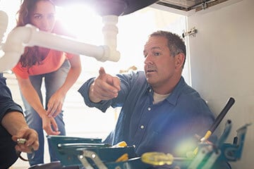 Plumber pointing out a problem with a pipe to a homeowner or tenant standing behind him
