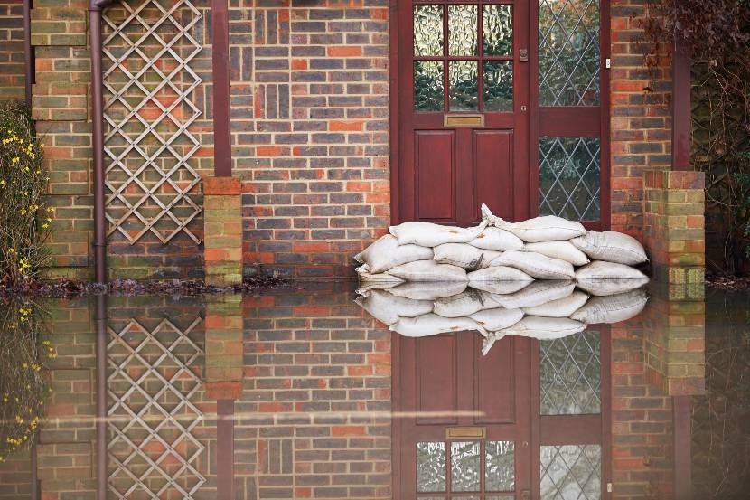 A series of sandbags packed up in front of a house door where flood water is rising