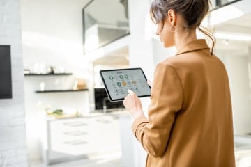  Person controlling smart home devices using a digital tablet with launched application in the white living room