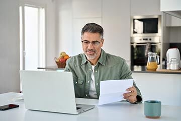 Man sat looking at a laptop holding a piece of paper